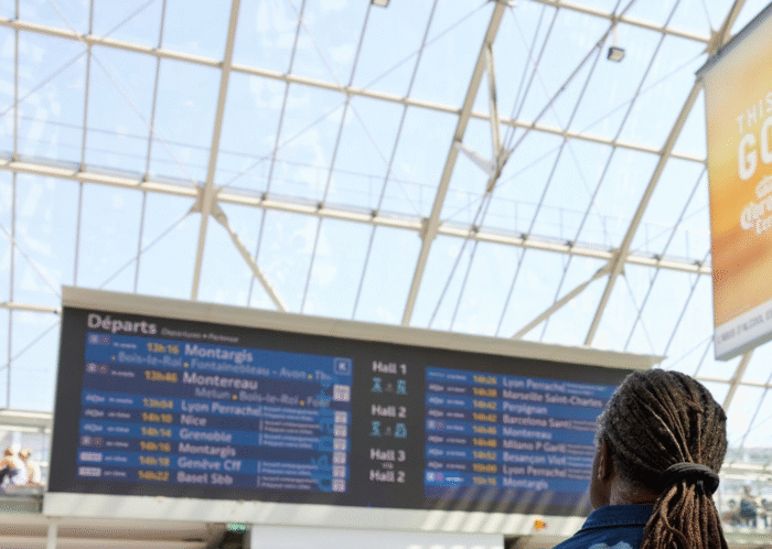 Photo d'un voyageur regardant les horaires sur un écran d'information en gare.